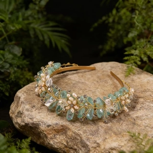 Detail of handmade gold crown with green crystals and pearls on a forest moss background