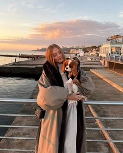 Parka invernale beige oversize con collo di pelliccia indossato da una donna al tramonto