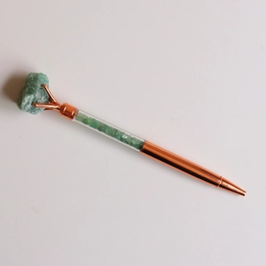 Detailed macro view of rose gold ballpoint pen with green raw stone and crystal chips