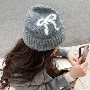 Close-up of deep gray knit beanie featuring white bow pattern and thick knit texture