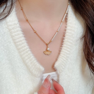 Close-up of maple leaf and pearl necklace with gold chain on model's neck