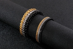 Close-up of Franco chain bracelets in gold, silver, and black on a textured display