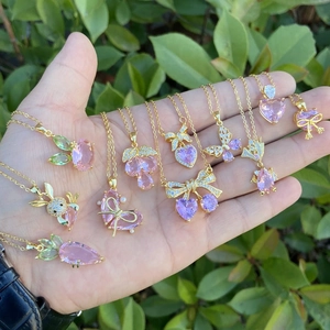 Pink butterfly and heart pendants on 18k gold plated necklaces held by hand