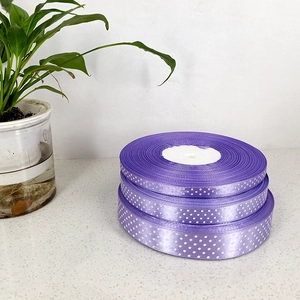 Three stacked rolls of purple grosgrain ribbon with white polka dots on a stone base