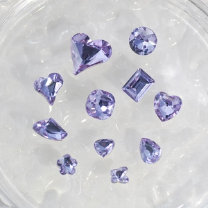 Sparkling purple K9 crystal nail art gems in various shapes on a textured surface
