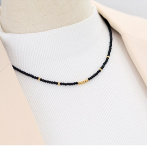 Detail of beaded necklace with black beads and gold accents worn on a white turtleneck
