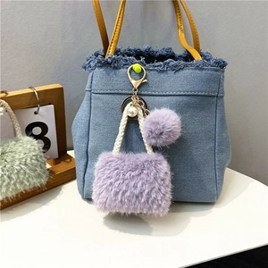 Close-up of purple faux fur mini bag keychain with pearl charm on denim background