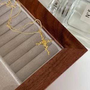 Close-up of golden cross rose pendant necklace displayed in a luxury grey jewelry box