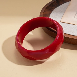 Detail of red resin wide bangle with unique irregular wavy texture and glossy finish