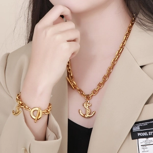 Fashionable golden anchor pendant necklace and bracelet set displayed on a female model