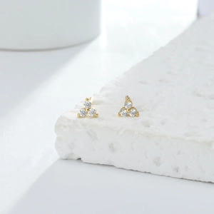 Macro shot of gold-plated cluster stud earrings featuring three white round-cut gemstones