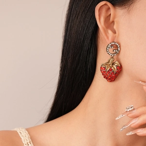 Close-up of red rhinestone strawberry earrings with vintage gold G-logo on a model