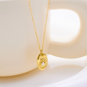 Vue détaillée du pendentif coquillage doré avec perle sur un bord de tasse blanche