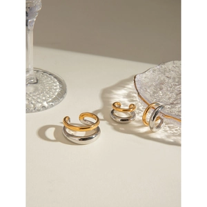 Polished two-tone double layer stainless steel ear cuffs on a light cream surface