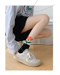Close-up of crew socks featuring red tulip floral pattern and vintage sneakers on wood floor