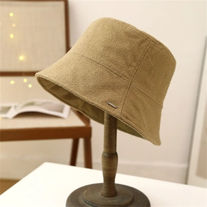 Chic camel wool bucket hat with decorative metal plate on a wooden stand