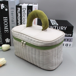 Quilted beige cosmetic bag with green handles and zippers in a minimalist scene