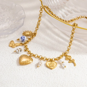 Collier vintage doré avec pendentifs soleil, papillon et médaillon cœur sur socle blanc