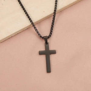 Detailed view of a matte black cross pendant on a sleek box chain over beige fabric