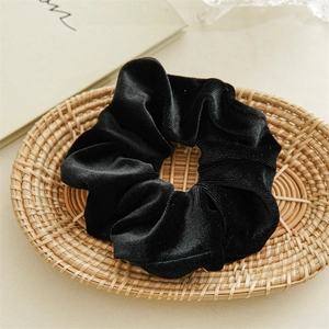 Λεπτομέρεια μαύρου βελούδινου scrunchie με ανάγλυφη υφή σε ψάθινο δίσκο