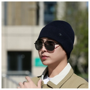 Detail of navy ribbed knit beanie with metallic side emblem on male model in city
