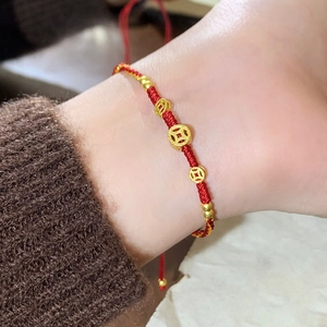 Gros plan sur un bracelet tressé rouge avec trois breloques pièces dorées au poignet