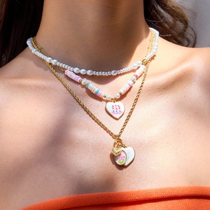 Détail de colliers dorés superposés avec pendentifs cœur, perles et billes colorées