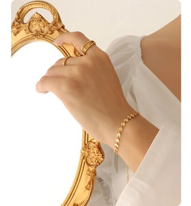 Detail of gold-plated sequin chain bracelet and layered rings on a female model