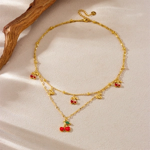 Double-layer gold plated stainless steel necklace with red cherry pendants on textured background