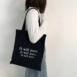 Minimalistische schwarze Canvas-Einkaufstasche mit weißem Schriftzug am Model getragen