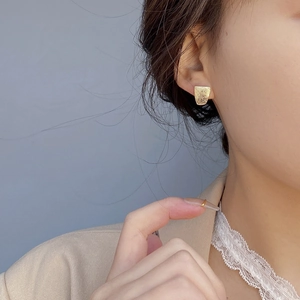 Macro shot of gold irregular trapezoid stud earrings with textured hammered finish