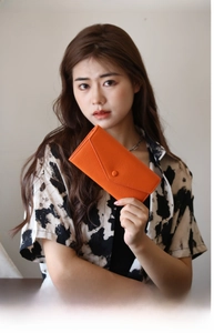 Orangefarbene lange Lederbrieftasche im Umschlag-Stil, von einem Model in der Hand gehalten