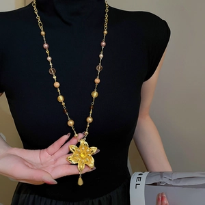 Détail d'un pendentif fleur dorée vintage et d'un long collier de perles sur pull noir