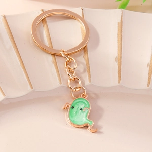 Close-up of cute green enamel ghost charm on a golden metal keychain over white ceramic