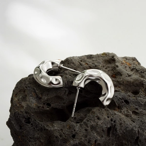 Detailed close-up of silver irregular hammered C-shape earrings on dark volcanic rock