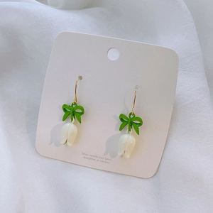 Close-up of tulip drop earrings with green bows and white flower buds on display card
