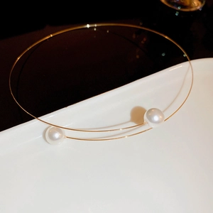 Close-up of minimalist gold wire necklace with white pearls on a white ceramic plate
