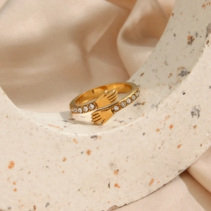 Detail of gold hugging hands ring with sparkling zircon crystals on silk background