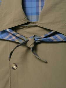Dettaglio giacca verde oliva con colletto a sciarpa e cintura in motivo scozzese blu marrone