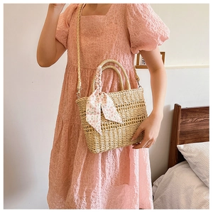 Detail of woven straw handbag with a floral pink ribbon on the handle shown by a model