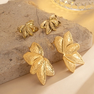 Gold plated leaf earrings with textured vein patterns on a natural stone base