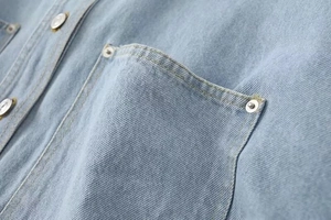 Close-up of front pocket on light blue denim shirt with durable double stitching