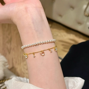 Close-up of heart-shaped jade pendants on gold chain and pearl bracelets on wrist
