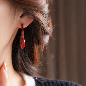 Close-up of a model wearing glossy red lava drip earrings in a minimalist fluid design