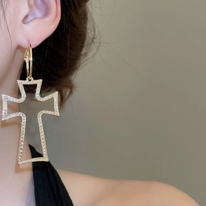 Close-up of a large golden hollow cross pendant earring with unique hammered texture
