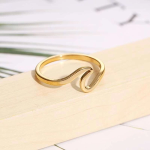 Macro shot of minimalist gold wave-shaped stainless steel ring on natural background