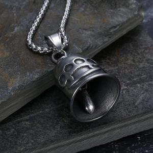Close-up of a punk style bell pendant with brass knuckles pattern on a rocky texture