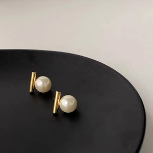 Nahaufnahme minimalistischer Perlenohrstecker mit Goldfinish auf schwarzem Display