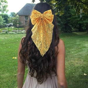 Détail d'une pince à cheveux à nœud en paillettes jaunes sur de longs cheveux ondulés