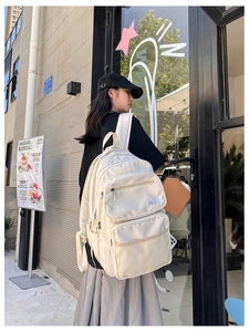 Detail view of cream white multi-pocket backpack showing side storage and durable fabric